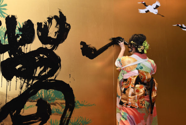 Shoran performing shodo on gold wall canvas in kimono